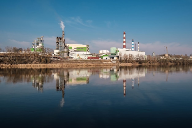 Tubos de serraria de fábrica de marcenaria perto do rio Conceito de poluição do ar Paisagem industrial poluição ambiental resíduos de usina termelétrica