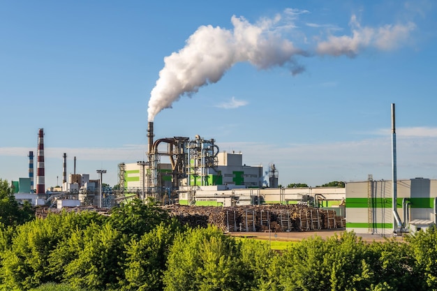 Tubos de serraria de planta de empresa de marcenaria com belo reflexo na água azul do rio Conceito de poluição do ar Paisagem industrial poluição ambiental resíduos de usina termelétrica