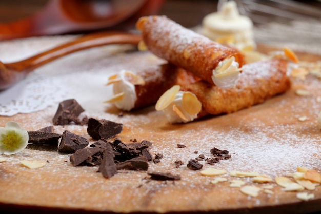 Tubos de wafer com creme e chocolate em uma bandeja de madeira com açúcar de confeiteiro