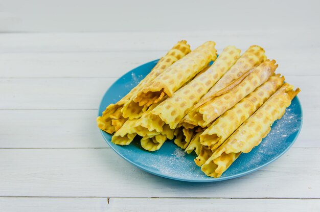 Tubos de waffle caseiros em uma placa azul sobre fundo branco com espaço de cópia