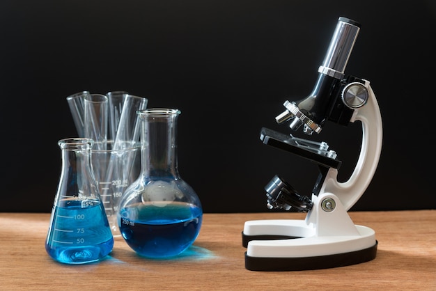 tubos de ensayo de laboratorio de ciencia y microscopio blanco en la mesa de madera con fondo negro