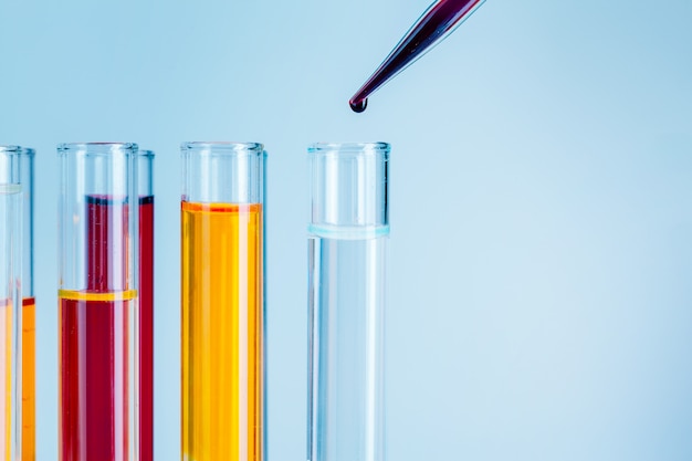 Tubos de ensayo de laboratorio con líquidos rojos y amarillos sobre fondo azul claro
