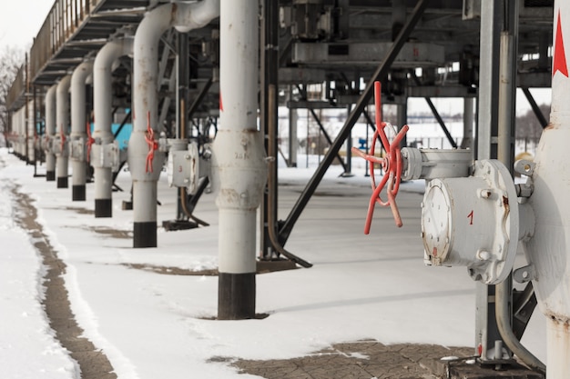 Los tubos de metal gris para el suministro de gas con válvulas rojas en la estación de compresores de gas se dispararon en invierno. La vista de una construcción de tubo para el transporte de gas en la estación de compresión de gas