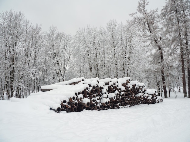 Tubos metálicos de gran diámetro para colocar comunicaciones, sistemas de drenaje y tuberías de calefacción debajo de la carretera, apilados al aire libre entre ventisqueros bajo una capa de nieve.