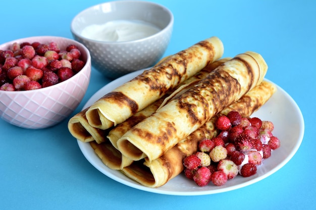 tubos de panqueques con fresas silvestres en el plato blanco sobre el fondo azul