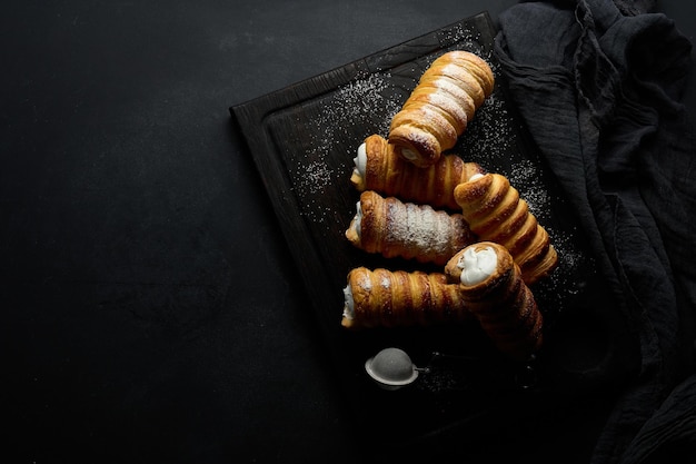 Túbulos horneados rellenos de crema de clara de huevo batida en una vista superior de tablero de cocina de madera negra