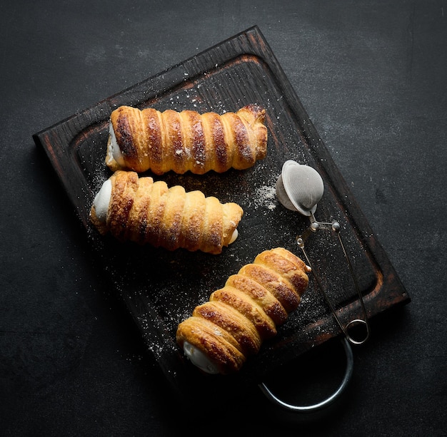 Túbulos horneados rellenos de crema de clara de huevo batida en una vista superior de tablero de cocina de madera negra