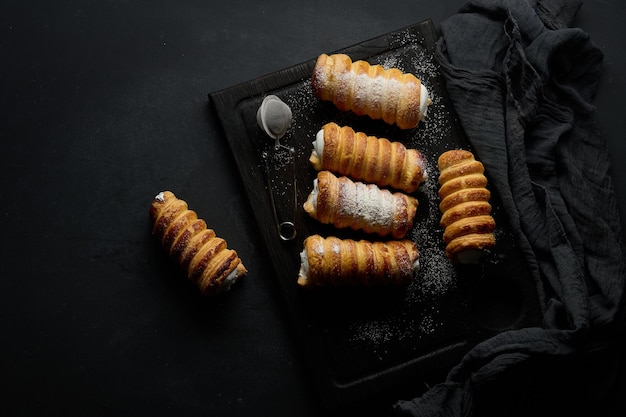 Túbulos horneados rellenos de crema de clara de huevo batida en una vista superior de tablero de cocina de madera negra