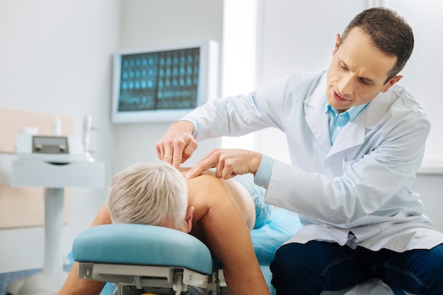 Tudo bem. bom médico inteligente e amigável olhando para seu paciente e fazendo uma pergunta enquanto verifica sua coluna