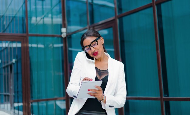 Tudo no trabalho. Mulher de negócios jovem afro falando ao telefone e escrevendo informações importantes no caderno