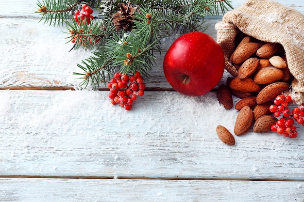 Tuercas con ramita de árbol de Navidad y manzana en cubierto con fondo de madera de color nieve