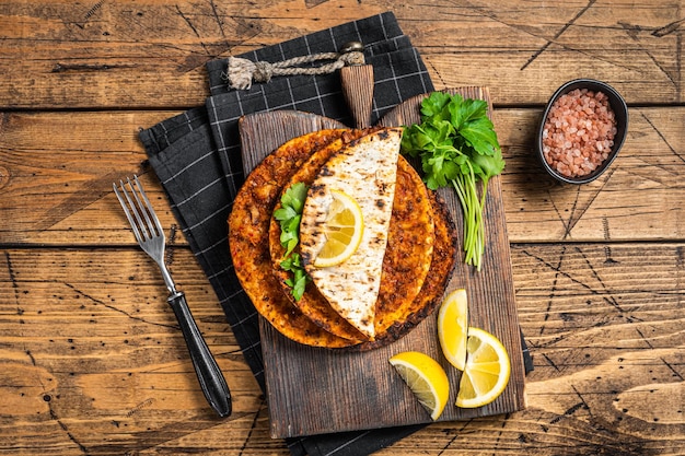 Türkische Küche mit dünnem Teig und Rinderhackfleisch lahmacun auf Holzbrett mit Kräutern Holzhintergrund Draufsicht