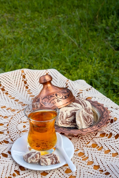 Türkischer Tee in einer Glasschale und Marmorhalva auf einem Tisch mit einer handgefertigten Tischdecke und einem Süßigkeitenhersteller