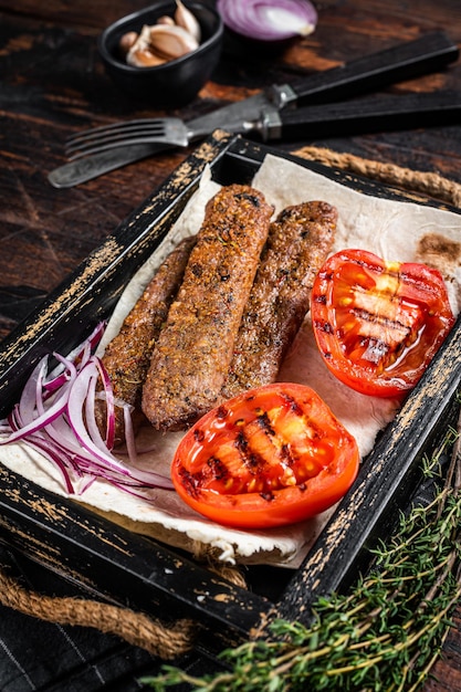 Türkischer Urfa-Kebab in einem Holztablett mit Brot, Zwiebeln und Tomaten. Hölzerner Hintergrund. Ansicht von oben.