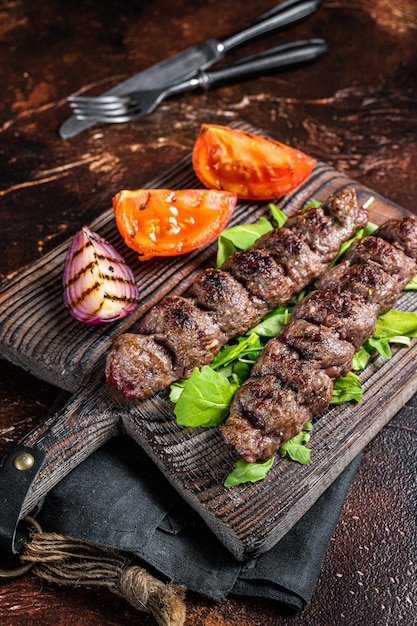 Foto türkisches adana-kebab-hackfleisch und lammfleisch am spieß gegrillt, serviert mit tomatensalat und zwiebeln dunkler hintergrund draufsicht