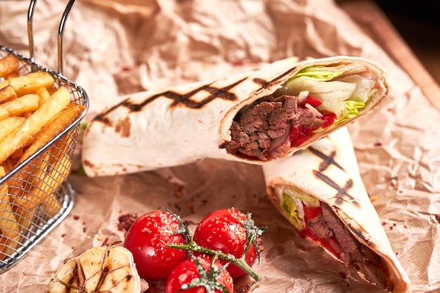 Türkisches Shawarma mit Rindfleisch und gebraten mit Tomaten auf Bastelpapier auf Holzplatte Fast-Food-Set Detailansicht
