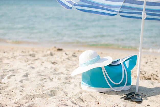 Türkisfarbene Tasche und weißer Hut am Strand.