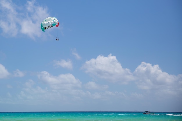 Türkisfarbenes Meer und ein Parasailing-Fallschirm mit Zeichen Mexiko und Farben der Flagge dieses Landes über dem karibischen Meer