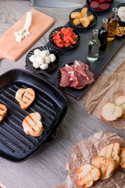 Tueste el pan en la cacerola de la parrilla cerca de la placa con la mozzarella y el jamón. Foto entonada. Bruschetta ingrediente.