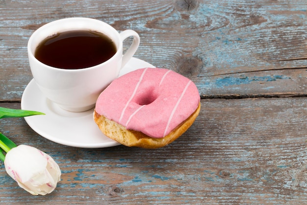 Tulipán blanco fresco y taza de café con donut sobre fondo de madera con espacio para copiar.