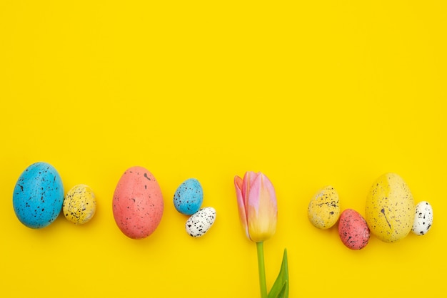 Un tulipán y huevos coloridos se encuentran en el fondo amarillo de Pascua, copyspace