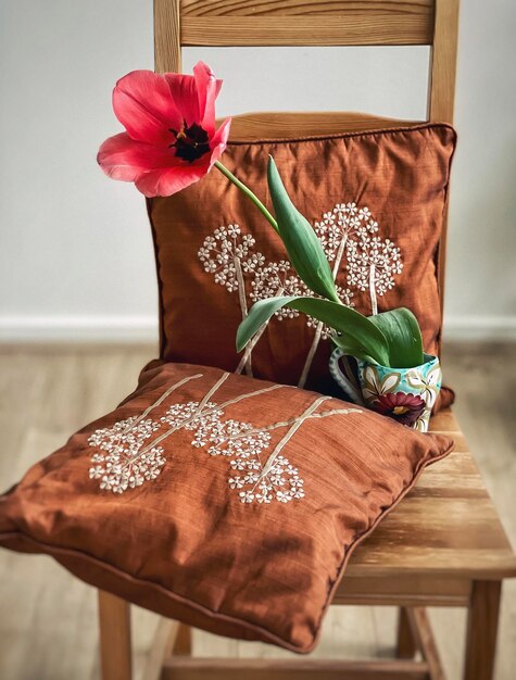 Foto tulipán rosa en jarrón vintage en silla de madera con cojines bordados marrones