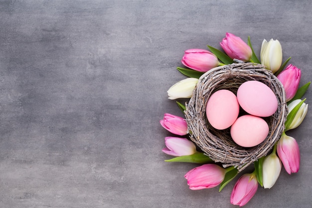 Tulipán rosa con nido de huevos de color rosa sobre un fondo gris. Tarjeta de saludos de Pascua.