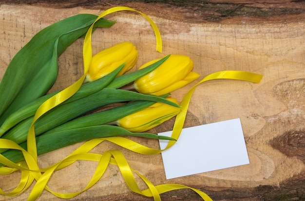 Tulipanes amarillos frescos con una cinta sobre una tabla de madera natural.