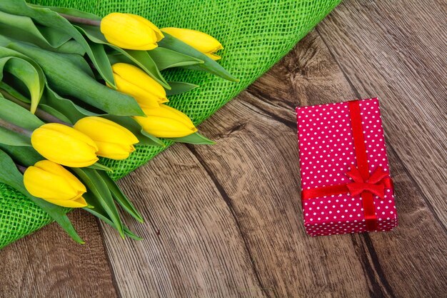 Tulipanes amarillos y regalo en una mesa de madera.