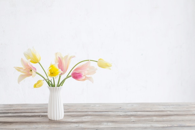 Tulipanes amarillos y rosados en un jarrón en la superficie de la pared blanca antigua