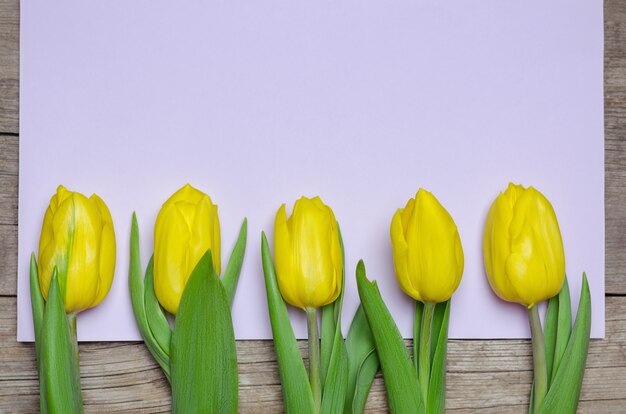 Tulipanes amarillos y tarjeta de color púrpura claro en la mesa de madera