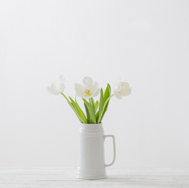 Tulipanes blancos en jarra sobre fondo blanco.