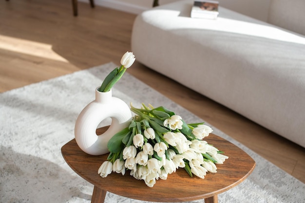 Tulipanes blancos en un jarrón moderno en una mesa de madera con sofá en el fondo