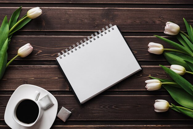 Tulipanes blancos en una mesa de madera con una taza de café y un cuaderno vacío