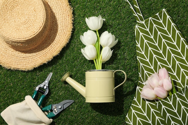 Los tulipanes en delantal y el riego pueden herramientas de jardinería y sombrero en el fondo verde vista superior