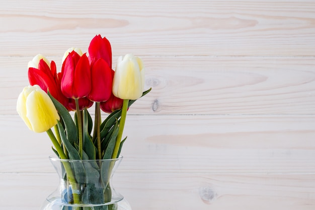 Tulipanes en un florero sobre un fondo claro de la madera. Tarjeta de regalo con espacio de texto, marco floral.