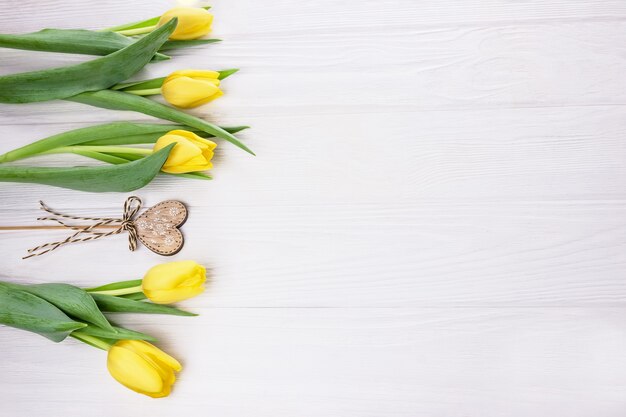 Tulipanes de flores amarillas y corazón de madera en un palo con un lazo