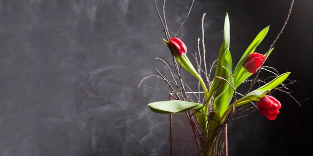 Los tulipanes hermosos florecen color rojo en el florero de cristal en fondo negro. Tarjeta de felicitación del día de San Valentín o día de la madre. Copiar espacio para texto. Bandera