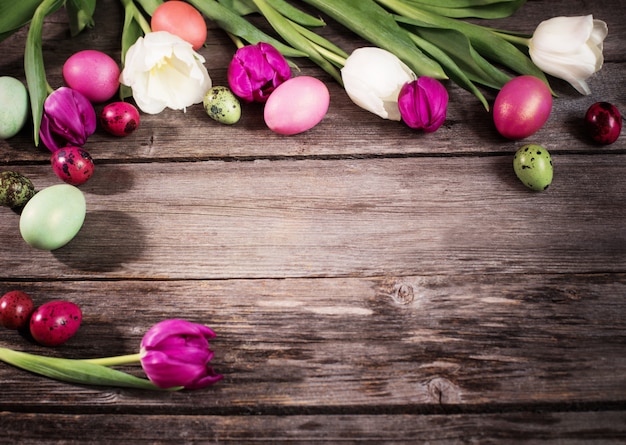 Tulipanes y huevos de pascua sobre fondo de madera