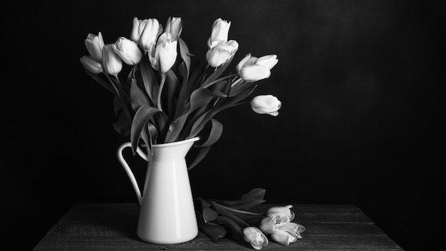 Tulipanes en una jarra sobre fondo oscuro en blanco y negro