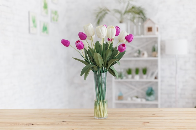 Tulipanes en un jarrón sobre una mesa de madera. Interior escandinavo.