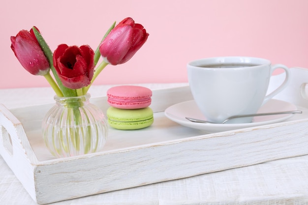 Foto tulipanes en macarrones de jarrón de vidrio y taza de café o té en bandeja de madera blanca