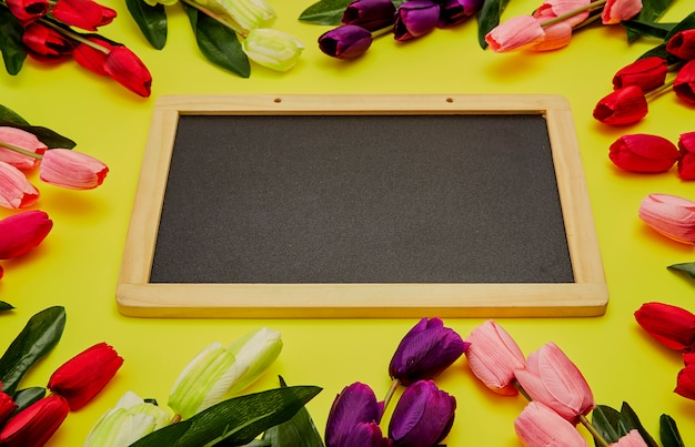 Tulipanes en mesa de madera con pizarra vacía negra