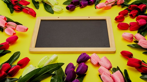 Tulipanes en mesa de madera con pizarra vacía negra