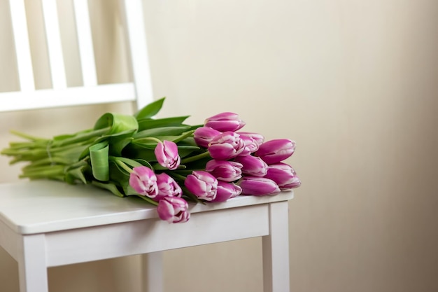 Los tulipanes morados yacen en una silla blanca en una habitación cerca de una pared clara