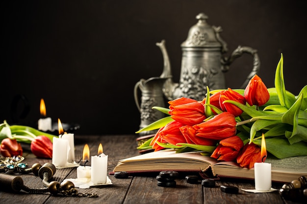 Tulipanes naranjas en libro antiguo con velas encendidas con una silueta en el humo. Cumpleaños, concepto de tarjeta de felicitación del día de la madre con espacio de copia