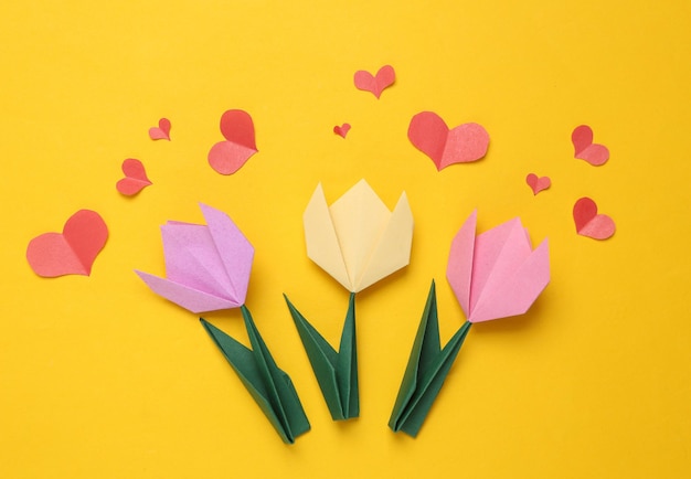 Tulipanes de papel de origami hechos a mano y corazones cortados en papel sobre fondo amarillo 8 de marzo o concepto del día de la madre Vista superior Minimalismo