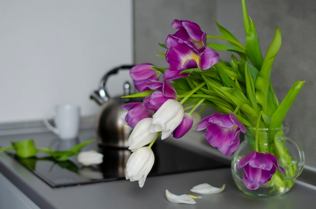 Tulipanes púrpuras y blancos en un florero transparente en una tabla de cocina. Buen comienzo del día.