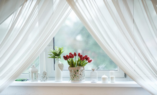 Tulipanes rojos y campanillas en una cesta en el alféizar de la ventana