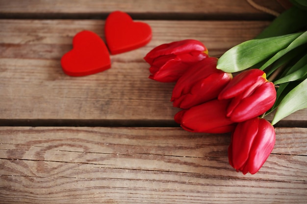 Tulipanes rojos con corazones decorativos en una mesa de madera de cerca